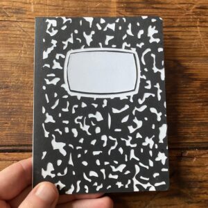composition-notebook-clipart-a-hand-holding-black-and-white-notebook-with-paper